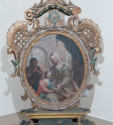 Zdjęcie nr 1: Pole obrazowe w formie stojącego owalu, ujęte profilowaną ramą dekorowaną rocaille'ową falbaną. Po bokach uszaki utworzone z wolut, rocaille'u i kratki regencyjnej, przechodzące w szczyt w formie uproszczonego baldachimu z cokołem zwieńczonym sercem, zdobionego wolutami i ornamentem roślinnym. Pod baldachimem medalion z monogramem Marii w glorii. Pole obrazowe ustawione na cokole o wolutowym kształcie nóżek i fantazyjnie wyciętej dolnej krawędzi, zamkniętym fragmentem gzymsu. W jego polu otwory na drążki. 
Na obrazie Nauczania Marii w centrum ukazana siedząca św. Anna, zwrócona w trzech czwartych w prawo, z pochyloną głową. Lewą ręką obejmuje stojącą przy jej boku Marię, prawą wskazuje na księgę leżącą na jej kolanach. Twarz ma owalną, o małych oczach skierowanych w dół, małym nosie i ustach. Nad głową ma nimb. Ubrana jest w białą suknię spodnią i zieloną suknię wierzchnią oraz jasnobrązowy płaszcz, na głowie ma biały welon. Maria ukazana w półpostaci, zwrócona jest w trzech czwartych w lewo, pochylona, w obu wyciągniętych do przodu rękach trzyma otwartą księgę na kolanach św. Anny. Twarz ma owalną, o małych oczach skierowanych w dół, małym nosie i ustach, okoloną jasnymi włosami, upiętymi z tyłu głowy, wokół niej gloria promienista. Ubrana jest w jasnoczerwoną suknię i niebieski płaszcz. W lewej części obrazu, na drugim planie stoi św. Joachim, zwrócony w trzech czwartych w lewo, z obiema dłońmi opartymi na lasce. Twarz ma owalną, o małych oczach skierowanych w dół, małym nosie i ustach, okoloną siwą brodą. Na głowie ma niebieskie nakrycie, a wokół niej nimb. Ubrany jest w jasnofioletową tunikę i niebieski płaszcz. Postacie ukazane na tle wnętrza z widocznymi arkadami. W prawej części obrazu kolumny zakryte ciemnoniebieską draperią, obszytą frędzlą, z chwostami. 
Na obrazie św. Alojzego w centrum ukazany święty w półpostaci, zwrócony profilem w prawo, pochylony nad stołem. W lewej, uniesionej ręce trzyma krucyfiks i białą tkaninę, prawa leży na stole, w dłoni trzyma dyscyplinę. Twarz ma pełną, o dużych, okrągłych oczach skierowanych w dół, dużym, garbatym nosie, pełnych ustach i wystającej brodzie. Włosy krótkie, brązowe. Ubrany jest w czarną sutannę. Stół nakryty jest czerwoną tkaniną, leży na nim czaszka, lilia i korona otwarta. Święty ukazany na tle nieba, wypełnionego obłokami, na którego tle unoszą się dwie grupy uskrzydlonych główek anielskich.

