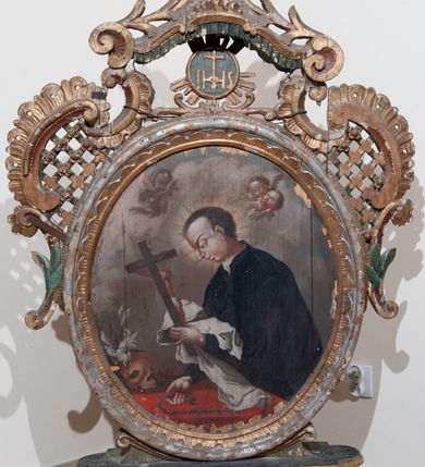 Zdjęcie nr 13: Pole obrazowe w formie stojącego owalu, ujęte profilowaną ramą dekorowaną rocaille'ową falbaną. Po bokach uszaki utworzone z wolut, rocaille'u i kratki regencyjnej, przechodzące w szczyt w formie uproszczonego baldachimu z cokołem zwieńczonym sercem, zdobionego wolutami i ornamentem roślinnym. Pod baldachimem medalion z monogramem Marii w glorii. Pole obrazowe ustawione na cokole o wolutowym kształcie nóżek i fantazyjnie wyciętej dolnej krawędzi, zamkniętym fragmentem gzymsu. W jego polu otwory na drążki. 
Na obrazie Nauczania Marii w centrum ukazana siedząca św. Anna, zwrócona w trzech czwartych w prawo, z pochyloną głową. Lewą ręką obejmuje stojącą przy jej boku Marię, prawą wskazuje na księgę leżącą na jej kolanach. Twarz ma owalną, o małych oczach skierowanych w dół, małym nosie i ustach. Nad głową ma nimb. Ubrana jest w białą suknię spodnią i zieloną suknię wierzchnią oraz jasnobrązowy płaszcz, na głowie ma biały welon. Maria ukazana w półpostaci, zwrócona jest w trzech czwartych w lewo, pochylona, w obu wyciągniętych do przodu rękach trzyma otwartą księgę na kolanach św. Anny. Twarz ma owalną, o małych oczach skierowanych w dół, małym nosie i ustach, okoloną jasnymi włosami, upiętymi z tyłu głowy, wokół niej gloria promienista. Ubrana jest w jasnoczerwoną suknię i niebieski płaszcz. W lewej części obrazu, na drugim planie stoi św. Joachim, zwrócony w trzech czwartych w lewo, z obiema dłońmi opartymi na lasce. Twarz ma owalną, o małych oczach skierowanych w dół, małym nosie i ustach, okoloną siwą brodą. Na głowie ma niebieskie nakrycie, a wokół niej nimb. Ubrany jest w jasnofioletową tunikę i niebieski płaszcz. Postacie ukazane na tle wnętrza z widocznymi arkadami. W prawej części obrazu kolumny zakryte ciemnoniebieską draperią, obszytą frędzlą, z chwostami. 
Na obrazie św. Alojzego w centrum ukazany święty w półpostaci, zwrócony profilem w prawo, pochylony nad stołem. W lewej, uniesionej ręce trzyma krucyfiks i białą tkaninę, prawa leży na stole, w dłoni trzyma dyscyplinę. Twarz ma pełną, o dużych, okrągłych oczach skierowanych w dół, dużym, garbatym nosie, pełnych ustach i wystającej brodzie. Włosy krótkie, brązowe. Ubrany jest w czarną sutannę. Stół nakryty jest czerwoną tkaniną, leży na nim czaszka, lilia i korona otwarta. Święty ukazany na tle nieba, wypełnionego obłokami, na którego tle unoszą się dwie grupy uskrzydlonych główek anielskich.

