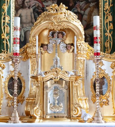 Zdjęcie nr 29: Nastawa architektoniczna, dwukondygnacyjna, pierwsza kondygnacja trójosiowa, druga jednoosiowa, z bramkami, ustawiona na cokole z wyodrębnionymi prostopadłościanami. Ołtarz murowany, w drewnianej obudowie, mensa drewniana. Boki ołtarza dekorowane malowanymi przedstawieniami nawiązującymi do alegorii Eucharystii, na prawym stół pokładny z chlebami pokładnymi, na lewym menora. Antepedium ujęte ramą, w polu trzy owalne pola, w środkowym ukazany Przybytek Świątyni Jerozolimskiej, w prawym ołtarz ofiary całopalnej, w lewym Arka Przymierza. Pola ujęte są malowanymi gałązkami oliwnymi. Oś środkowa pierwszej kondygnacji wydzielona parą kolumn o kapitelach kompozytowych, dźwigających pełne belkowanie, nad polem głównym wyłamane na kształt łuku odcinkowego, z przerwanym architrawem. Na belkowaniu fragmenty przerwanego półkolistego przyczółka z cokołami na figury św. Jadwigi Śląskiej i św. Elżbiety oraz rzeźby klęczących aniołów. Fryz dekorowany stylizowaną małżowiną i uskrzydlonymi główkami anielskimi. W polu środkowym wnęka w formie stojącego prostokąta zamkniętego łukiem odcinkowym, ujęta wąską ramą, flankowana lizenami zdobionymi wicią winnego grona. W polu obraz Wszystkich Świętych adorujących Trójcę Świętą. Na osiach bocznych nisze z konchami zdobionymi stylizowaną małżowiną, w których na wspornikach stoją figury św. Filipa i św. Jakuba Większego. Kondygnacja ujęta uszami utworzonymi z ornamentu małżowinowo-chrząstkowego i uskrzydlonych główek anielskich z czubami. 
Druga kondygnacja ustawiona na cokole, flankowana parą kolumn dźwigających pełne belkowanie, wyłamane na ich osi, oraz fragmenty zdwojonego, przerwanego, trójkątnego przyczółka z cokołami na figury św. Szczepana i św. Wawrzyńca. Fryz dekorowany małżowiną, rautami i uskrzydloną główką anielską. W centralnym punkcie belkowania cokół zakończony gzymsem, dekorowanym uskrzydloną główką anielską, z figurą św. Michała Archanioła. W polu głęboka wnęka w formie kwadratu, zamkniętego z dwóch stron łukami odcinkowymi nadwieszonymi, ujęta profilowaną ramą, z figurą Marki Boskiej Niepokalanie Poczętej, w glorii promienistej. Pole dekorowane małżowiną. 
Bramki umieszczone w przestrzeni dobudowanego do nastawy cokołu, wyodrębnione z niego. Przejścia w formie stojącego prostokąta zamkniętego łukiem półkolistym nadwieszonym, flankowane stylizowanymi pilastrami o trzonach dekorowanych stylizowaną wstęgą z akantem, dźwigającymi imposty zdobione rozetami. Na bramkach, na niskich cokołach małe aedicule z konchami, ujęte parami półkolumienek, dekorowane z trzech stron wstęgą z akantem przechodzącą w rogi obfitości z kampanulami oraz wicią roślinną z anthemionem. W aediculach figury św. Piotra i św. Pawła. Drzwiczki z malowanymi przedstawieniami św. Katarzyny Aleksandryjskiej  i św. Barbary. Struktura polichromowana w sposób imitujący marmoryzację w różnych odcieniach zieleni, kolumny, ornamentyka i profile złocone. 

