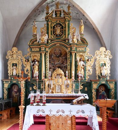 Zdjęcie nr 1: Nastawa architektoniczna, dwukondygnacyjna, pierwsza kondygnacja trójosiowa, druga jednoosiowa, z bramkami, ustawiona na cokole z wyodrębnionymi prostopadłościanami. Ołtarz murowany, w drewnianej obudowie, mensa drewniana. Boki ołtarza dekorowane malowanymi przedstawieniami nawiązującymi do alegorii Eucharystii, na prawym stół pokładny z chlebami pokładnymi, na lewym menora. Antepedium ujęte ramą, w polu trzy owalne pola, w środkowym ukazany Przybytek Świątyni Jerozolimskiej, w prawym ołtarz ofiary całopalnej, w lewym Arka Przymierza. Pola ujęte są malowanymi gałązkami oliwnymi. Oś środkowa pierwszej kondygnacji wydzielona parą kolumn o kapitelach kompozytowych, dźwigających pełne belkowanie, nad polem głównym wyłamane na kształt łuku odcinkowego, z przerwanym architrawem. Na belkowaniu fragmenty przerwanego półkolistego przyczółka z cokołami na figury św. Jadwigi Śląskiej i św. Elżbiety oraz rzeźby klęczących aniołów. Fryz dekorowany stylizowaną małżowiną i uskrzydlonymi główkami anielskimi. W polu środkowym wnęka w formie stojącego prostokąta zamkniętego łukiem odcinkowym, ujęta wąską ramą, flankowana lizenami zdobionymi wicią winnego grona. W polu obraz Wszystkich Świętych adorujących Trójcę Świętą. Na osiach bocznych nisze z konchami zdobionymi stylizowaną małżowiną, w których na wspornikach stoją figury św. Filipa i św. Jakuba Większego. Kondygnacja ujęta uszami utworzonymi z ornamentu małżowinowo-chrząstkowego i uskrzydlonych główek anielskich z czubami. 
Druga kondygnacja ustawiona na cokole, flankowana parą kolumn dźwigających pełne belkowanie, wyłamane na ich osi, oraz fragmenty zdwojonego, przerwanego, trójkątnego przyczółka z cokołami na figury św. Szczepana i św. Wawrzyńca. Fryz dekorowany małżowiną, rautami i uskrzydloną główką anielską. W centralnym punkcie belkowania cokół zakończony gzymsem, dekorowanym uskrzydloną główką anielską, z figurą św. Michała Archanioła. W polu głęboka wnęka w formie kwadratu, zamkniętego z dwóch stron łukami odcinkowymi nadwieszonymi, ujęta profilowaną ramą, z figurą Marki Boskiej Niepokalanie Poczętej, w glorii promienistej. Pole dekorowane małżowiną. 
Bramki umieszczone w przestrzeni dobudowanego do nastawy cokołu, wyodrębnione z niego. Przejścia w formie stojącego prostokąta zamkniętego łukiem półkolistym nadwieszonym, flankowane stylizowanymi pilastrami o trzonach dekorowanych stylizowaną wstęgą z akantem, dźwigającymi imposty zdobione rozetami. Na bramkach, na niskich cokołach małe aedicule z konchami, ujęte parami półkolumienek, dekorowane z trzech stron wstęgą z akantem przechodzącą w rogi obfitości z kampanulami oraz wicią roślinną z anthemionem. W aediculach figury św. Piotra i św. Pawła. Drzwiczki z malowanymi przedstawieniami św. Katarzyny Aleksandryjskiej  i św. Barbary. Struktura polichromowana w sposób imitujący marmoryzację w różnych odcieniach zieleni, kolumny, ornamentyka i profile złocone. 

