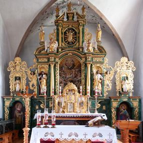 Zdjęcie nr 1: Nastawa architektoniczna, dwukondygnacyjna, pierwsza kondygnacja trójosiowa, druga jednoosiowa, z bramkami, ustawiona na cokole z wyodrębnionymi prostopadłościanami. Ołtarz murowany, w drewnianej obudowie, mensa drewniana. Boki ołtarza dekorowane malowanymi przedstawieniami nawiązującymi do alegorii Eucharystii, na prawym stół pokładny z chlebami pokładnymi, na lewym menora. Antepedium ujęte ramą, w polu trzy owalne pola, w środkowym ukazany Przybytek Świątyni Jerozolimskiej, w prawym ołtarz ofiary całopalnej, w lewym Arka Przymierza. Pola ujęte są malowanymi gałązkami oliwnymi. Oś środkowa pierwszej kondygnacji wydzielona parą kolumn o kapitelach kompozytowych, dźwigających pełne belkowanie, nad polem głównym wyłamane na kształt łuku odcinkowego, z przerwanym architrawem. Na belkowaniu fragmenty przerwanego półkolistego przyczółka z cokołami na figury św. Jadwigi Śląskiej i św. Elżbiety oraz rzeźby klęczących aniołów. Fryz dekorowany stylizowaną małżowiną i uskrzydlonymi główkami anielskimi. W polu środkowym wnęka w formie stojącego prostokąta zamkniętego łukiem odcinkowym, ujęta wąską ramą, flankowana lizenami zdobionymi wicią winnego grona. W polu obraz Wszystkich Świętych adorujących Trójcę Świętą. Na osiach bocznych nisze z konchami zdobionymi stylizowaną małżowiną, w których na wspornikach stoją figury św. Filipa i św. Jakuba Większego. Kondygnacja ujęta uszami utworzonymi z ornamentu małżowinowo-chrząstkowego i uskrzydlonych główek anielskich z czubami. 
Druga kondygnacja ustawiona na cokole, flankowana parą kolumn dźwigających pełne belkowanie, wyłamane na ich osi, oraz fragmenty zdwojonego, przerwanego, trójkątnego przyczółka z cokołami na figury św. Szczepana i św. Wawrzyńca. Fryz dekorowany małżowiną, rautami i uskrzydloną główką anielską. W centralnym punkcie belkowania cokół zakończony gzymsem, dekorowanym uskrzydloną główką anielską, z figurą św. Michała Archanioła. W polu głęboka wnęka w formie kwadratu, zamkniętego z dwóch stron łukami odcinkowymi nadwieszonymi, ujęta profilowaną ramą, z figurą Marki Boskiej Niepokalanie Poczętej, w glorii promienistej. Pole dekorowane małżowiną. 
Bramki umieszczone w przestrzeni dobudowanego do nastawy cokołu, wyodrębnione z niego. Przejścia w formie stojącego prostokąta zamkniętego łukiem półkolistym nadwieszonym, flankowane stylizowanymi pilastrami o trzonach dekorowanych stylizowaną wstęgą z akantem, dźwigającymi imposty zdobione rozetami. Na bramkach, na niskich cokołach małe aedicule z konchami, ujęte parami półkolumienek, dekorowane z trzech stron wstęgą z akantem przechodzącą w rogi obfitości z kampanulami oraz wicią roślinną z anthemionem. W aediculach figury św. Piotra i św. Pawła. Drzwiczki z malowanymi przedstawieniami św. Katarzyny Aleksandryjskiej  i św. Barbary. Struktura polichromowana w sposób imitujący marmoryzację w różnych odcieniach zieleni, kolumny, ornamentyka i profile złocone. 

