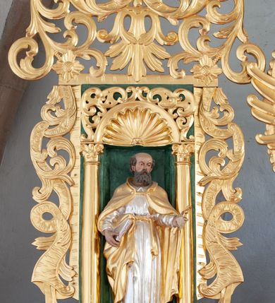Zdjęcie nr 15: Nastawa architektoniczna, dwukondygnacyjna, pierwsza kondygnacja trójosiowa, druga jednoosiowa, z bramkami, ustawiona na cokole z wyodrębnionymi prostopadłościanami. Ołtarz murowany, w drewnianej obudowie, mensa drewniana. Boki ołtarza dekorowane malowanymi przedstawieniami nawiązującymi do alegorii Eucharystii, na prawym stół pokładny z chlebami pokładnymi, na lewym menora. Antepedium ujęte ramą, w polu trzy owalne pola, w środkowym ukazany Przybytek Świątyni Jerozolimskiej, w prawym ołtarz ofiary całopalnej, w lewym Arka Przymierza. Pola ujęte są malowanymi gałązkami oliwnymi. Oś środkowa pierwszej kondygnacji wydzielona parą kolumn o kapitelach kompozytowych, dźwigających pełne belkowanie, nad polem głównym wyłamane na kształt łuku odcinkowego, z przerwanym architrawem. Na belkowaniu fragmenty przerwanego półkolistego przyczółka z cokołami na figury św. Jadwigi Śląskiej i św. Elżbiety oraz rzeźby klęczących aniołów. Fryz dekorowany stylizowaną małżowiną i uskrzydlonymi główkami anielskimi. W polu środkowym wnęka w formie stojącego prostokąta zamkniętego łukiem odcinkowym, ujęta wąską ramą, flankowana lizenami zdobionymi wicią winnego grona. W polu obraz Wszystkich Świętych adorujących Trójcę Świętą. Na osiach bocznych nisze z konchami zdobionymi stylizowaną małżowiną, w których na wspornikach stoją figury św. Filipa i św. Jakuba Większego. Kondygnacja ujęta uszami utworzonymi z ornamentu małżowinowo-chrząstkowego i uskrzydlonych główek anielskich z czubami. 
Druga kondygnacja ustawiona na cokole, flankowana parą kolumn dźwigających pełne belkowanie, wyłamane na ich osi, oraz fragmenty zdwojonego, przerwanego, trójkątnego przyczółka z cokołami na figury św. Szczepana i św. Wawrzyńca. Fryz dekorowany małżowiną, rautami i uskrzydloną główką anielską. W centralnym punkcie belkowania cokół zakończony gzymsem, dekorowanym uskrzydloną główką anielską, z figurą św. Michała Archanioła. W polu głęboka wnęka w formie kwadratu, zamkniętego z dwóch stron łukami odcinkowymi nadwieszonymi, ujęta profilowaną ramą, z figurą Marki Boskiej Niepokalanie Poczętej, w glorii promienistej. Pole dekorowane małżowiną. 
Bramki umieszczone w przestrzeni dobudowanego do nastawy cokołu, wyodrębnione z niego. Przejścia w formie stojącego prostokąta zamkniętego łukiem półkolistym nadwieszonym, flankowane stylizowanymi pilastrami o trzonach dekorowanych stylizowaną wstęgą z akantem, dźwigającymi imposty zdobione rozetami. Na bramkach, na niskich cokołach małe aedicule z konchami, ujęte parami półkolumienek, dekorowane z trzech stron wstęgą z akantem przechodzącą w rogi obfitości z kampanulami oraz wicią roślinną z anthemionem. W aediculach figury św. Piotra i św. Pawła. Drzwiczki z malowanymi przedstawieniami św. Katarzyny Aleksandryjskiej  i św. Barbary. Struktura polichromowana w sposób imitujący marmoryzację w różnych odcieniach zieleni, kolumny, ornamentyka i profile złocone. 

