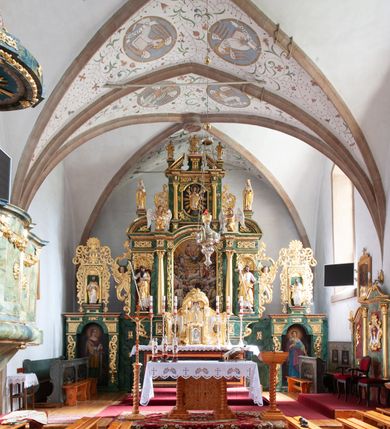 Zdjęcie nr 13: Nastawa architektoniczna, dwukondygnacyjna, pierwsza kondygnacja trójosiowa, druga jednoosiowa, z bramkami, ustawiona na cokole z wyodrębnionymi prostopadłościanami. Ołtarz murowany, w drewnianej obudowie, mensa drewniana. Boki ołtarza dekorowane malowanymi przedstawieniami nawiązującymi do alegorii Eucharystii, na prawym stół pokładny z chlebami pokładnymi, na lewym menora. Antepedium ujęte ramą, w polu trzy owalne pola, w środkowym ukazany Przybytek Świątyni Jerozolimskiej, w prawym ołtarz ofiary całopalnej, w lewym Arka Przymierza. Pola ujęte są malowanymi gałązkami oliwnymi. Oś środkowa pierwszej kondygnacji wydzielona parą kolumn o kapitelach kompozytowych, dźwigających pełne belkowanie, nad polem głównym wyłamane na kształt łuku odcinkowego, z przerwanym architrawem. Na belkowaniu fragmenty przerwanego półkolistego przyczółka z cokołami na figury św. Jadwigi Śląskiej i św. Elżbiety oraz rzeźby klęczących aniołów. Fryz dekorowany stylizowaną małżowiną i uskrzydlonymi główkami anielskimi. W polu środkowym wnęka w formie stojącego prostokąta zamkniętego łukiem odcinkowym, ujęta wąską ramą, flankowana lizenami zdobionymi wicią winnego grona. W polu obraz Wszystkich Świętych adorujących Trójcę Świętą. Na osiach bocznych nisze z konchami zdobionymi stylizowaną małżowiną, w których na wspornikach stoją figury św. Filipa i św. Jakuba Większego. Kondygnacja ujęta uszami utworzonymi z ornamentu małżowinowo-chrząstkowego i uskrzydlonych główek anielskich z czubami. 
Druga kondygnacja ustawiona na cokole, flankowana parą kolumn dźwigających pełne belkowanie, wyłamane na ich osi, oraz fragmenty zdwojonego, przerwanego, trójkątnego przyczółka z cokołami na figury św. Szczepana i św. Wawrzyńca. Fryz dekorowany małżowiną, rautami i uskrzydloną główką anielską. W centralnym punkcie belkowania cokół zakończony gzymsem, dekorowanym uskrzydloną główką anielską, z figurą św. Michała Archanioła. W polu głęboka wnęka w formie kwadratu, zamkniętego z dwóch stron łukami odcinkowymi nadwieszonymi, ujęta profilowaną ramą, z figurą Marki Boskiej Niepokalanie Poczętej, w glorii promienistej. Pole dekorowane małżowiną. 
Bramki umieszczone w przestrzeni dobudowanego do nastawy cokołu, wyodrębnione z niego. Przejścia w formie stojącego prostokąta zamkniętego łukiem półkolistym nadwieszonym, flankowane stylizowanymi pilastrami o trzonach dekorowanych stylizowaną wstęgą z akantem, dźwigającymi imposty zdobione rozetami. Na bramkach, na niskich cokołach małe aedicule z konchami, ujęte parami półkolumienek, dekorowane z trzech stron wstęgą z akantem przechodzącą w rogi obfitości z kampanulami oraz wicią roślinną z anthemionem. W aediculach figury św. Piotra i św. Pawła. Drzwiczki z malowanymi przedstawieniami św. Katarzyny Aleksandryjskiej  i św. Barbary. Struktura polichromowana w sposób imitujący marmoryzację w różnych odcieniach zieleni, kolumny, ornamentyka i profile złocone. 

