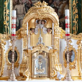 Zdjęcie nr 1: Tabernakulum w formie prostopadłościennej szafki na cokole, o wypukłej ścianie frontowej, ujętej spływami wolutowymi, podtrzymującymi wyłamany gzyms. Drzwiczki w kształcie stojącego prostokąta zamkniętego łukiem półkolistym nadwieszonym z uskokiem, ujęte profilowana ramą z przedstawieniem kielicha z hostią w polu. Na tabernakulum cokół. Szafka wkomponowana w trójosiowy tron wystawienia. Oś środkowa w formie niszy, flankowanej spływami wolutowymi, dekorowanej rocaille'm i uskrzydlonymi główkami anielskimi. Po bokach niszy, na osiach bocznych pola o wklęsłych bokach dekorowanych zwisami kwiatowymi, z umieszczonymi pośrodku owalnymi pojemnikami na relikwie ujętymi rocaille'm. Wnętrze pojemników z ornamentalną dekoracją papierową i banderolami oraz relikwiami. W prawym pojemniku napisy: „Innoc(enti) Pap(ae) IX.”, „Gregor(ii) Pap(ae) VII.”, „S(anctae) AUREAE M(artyris)”, „Clement(i) Pap(ae) XI.”, „Bened(icti) Pap(ae) XI.”; w lewym: „Pii. Pap(ae) V.”, „Clem(enti) Pap(ae) XII”, „S(ancti) Benigni(s) M(artyris)”, „Innoc(enti) Pap(ae) XIII.”, „Bened(icti) Pap(ae) XIII.”; „ST[...] VM.”

