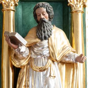 Zdjęcie nr 1: Figura ścięta z tyłu, ustawiona na niskiej podstawie. Święty ukazany frontalnie, w lekkim kontrapoście, z pochyloną głową skierowaną w prawo. Ręce ma ugięte i rozłożone na boki, w prawej podtrzymuje otwartą księgę. Twarz ma pociągłą, z dużymi oczami, skierowanymi w dół, uniesionymi brwiami, dużym nosem i małymi ustami, okoloną długą, falowaną brodą i krótkimi, kręconymi włosami. Ubrany jest w srebrzoną tunikę, przepasaną w talii oraz złocony płaszcz zarzucony na ramiona. Polichromia ciała naturalistyczna. 


