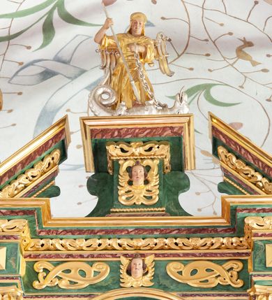 Zdjęcie nr 2: Figura ścięta z tyłu i drążona. Święty Michał Archanioł ukazany frontalnie, lewą nogą depcze srebrzonego smoka leżącego przed nim, w lewej ręce trzyma łańcuch z jego obroży, w prawej trzyma włócznię skierowaną ostrzem w dół. Twarz ma kwadratową, o wąskich oczach, małym nosie i ustach. Na głowie ma nakrycie. Ubrany jest w złoconą tunikę oraz zbroję. Skrzydła są srebrzone i złożone po bokach. Polichromia ciała naturalistyczna. 

