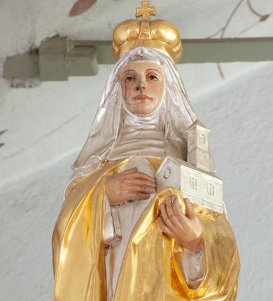 Zdjęcie nr 1: Figura ścięta z tyłu i drążona, ustawiona na niskiej podstawie. Święta ukazana frontalnie, w kontrapoście, lewą ręką podtrzymuje model świątyni, prawą kładzie na piersi. Twarz ma pociągłą, o migdałowatych oczach, małym nosie i dużych ustach. Ubrana jest w srebrzoną suknię, złocony płaszcz zarzucony na ramiona, wokół głowy ma srebrzoną podwikę i welon opadający na ramiona, na głowie złocona korona zamknięta. Polichromia ciała naturalistyczna. 

