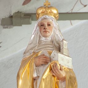 Zdjęcie nr 1: Figura ścięta z tyłu i drążona, ustawiona na niskiej podstawie. Święta ukazana frontalnie, w kontrapoście, lewą ręką podtrzymuje model świątyni, prawą kładzie na piersi. Twarz ma pociągłą, o migdałowatych oczach, małym nosie i dużych ustach. Ubrana jest w srebrzoną suknię, złocony płaszcz zarzucony na ramiona, wokół głowy ma srebrzoną podwikę i welon opadający na ramiona, na głowie złocona korona zamknięta. Polichromia ciała naturalistyczna. 

