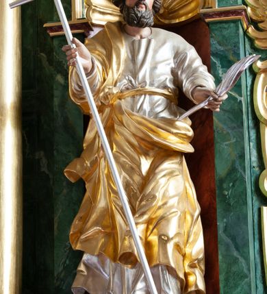 Zdjęcie nr 2: Figura ścięta z tyłu i drążona, ustawiona na niskiej podstawie w formie skały. Święty ukazany frontalnie, w kontrapoście, z głową skierowaną w lewo. Ręce ma wyciągnięte do przodu i rozłożone, w lewej dłoni ma pióro, w prawej trzyma laskę zakończoną krzyżem. Twarz ma pociągłą, o niskim czole, migdałowatych oczach, małym nosie i ustach, okoloną gęstą, silnie kręconą brodą oraz krótkimi skręconymi w pojedyncze pasma włosami. Ubrany jest w srebrzoną tunikę, przepasaną złoconą wstęgą w talii oraz złocony płaszcz zarzucony na prawe ramię i zawinięty z przodu postaci. Polichromia ciała naturalistyczna. 


