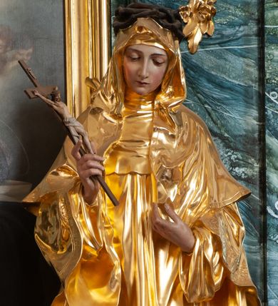 Zdjęcie nr 1: Rzeźba delikatnie ścięta z tyłu, ustawiona na niskiej podstawie. Święta ukazana frontalnie, w kontrapoście, z pochyloną głową, obie ręce ma ugięte i lekko uniesione, w prawej trzyma krucyfiks. Twarz ma owalną, o dużych oczach skierowanych w dół, prostym, wąskim nosie i ustach. Ubrana jest w złocony habit z pelerynką i szkaplerzem, złocony płaszcz o dekoracyjnej bordiurze narzucony na ramiona oraz złocony welon. Na głowie ma brązową koronę cierniową. Polichromia ciała naturalistyczna. 


