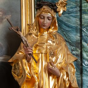 Zdjęcie nr 1: Rzeźba delikatnie ścięta z tyłu, ustawiona na niskiej podstawie. Święta ukazana frontalnie, w kontrapoście, z pochyloną głową, obie ręce ma ugięte i lekko uniesione, w prawej trzyma krucyfiks. Twarz ma owalną, o dużych oczach skierowanych w dół, prostym, wąskim nosie i ustach. Ubrana jest w złocony habit z pelerynką i szkaplerzem, złocony płaszcz o dekoracyjnej bordiurze narzucony na ramiona oraz złocony welon. Na głowie ma brązową koronę cierniową. Polichromia ciała naturalistyczna. 


