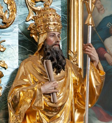 Zdjęcie nr 1: Rzeźba delikatnie ścięta z tyłu, ustawiona na niskiej podstawie. Święty zwrócony frontalnie, w kontrapoście, lewą ręką trzyma laskę zakończoną znakiem Chi Rho, w prawej, ugiętej trzyma zwój. Twarz ma pociągłą, o dużych, migdałowatych oczach, prostym nosie i małych ustach, okoloną gęstą, kręconą brodą, opadającą na pierś. Na głowie ma złoconą tiarę papieską. Ubrany jest w luźną, złoconą albę oraz złocony ornat o dekoracyjnej płaskorzeźbionej bordiurze. Polichromia ciała naturalistyczna. 