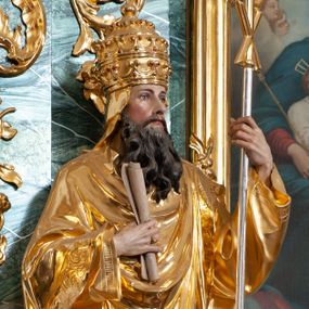 Zdjęcie nr 1: Rzeźba delikatnie ścięta z tyłu, ustawiona na niskiej podstawie. Święty zwrócony frontalnie, w kontrapoście, lewą ręką trzyma laskę zakończoną znakiem Chi Rho, w prawej, ugiętej trzyma zwój. Twarz ma pociągłą, o dużych, migdałowatych oczach, prostym nosie i małych ustach, okoloną gęstą, kręconą brodą, opadającą na pierś. Na głowie ma złoconą tiarę papieską. Ubrany jest w luźną, złoconą albę oraz złocony ornat o dekoracyjnej płaskorzeźbionej bordiurze. Polichromia ciała naturalistyczna. 