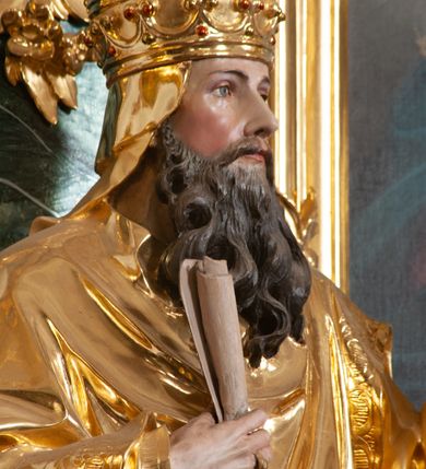 Zdjęcie nr 6: Rzeźba delikatnie ścięta z tyłu, ustawiona na niskiej podstawie. Święty zwrócony frontalnie, w kontrapoście, lewą ręką trzyma laskę zakończoną znakiem Chi Rho, w prawej, ugiętej trzyma zwój. Twarz ma pociągłą, o dużych, migdałowatych oczach, prostym nosie i małych ustach, okoloną gęstą, kręconą brodą, opadającą na pierś. Na głowie ma złoconą tiarę papieską. Ubrany jest w luźną, złoconą albę oraz złocony ornat o dekoracyjnej płaskorzeźbionej bordiurze. Polichromia ciała naturalistyczna. 