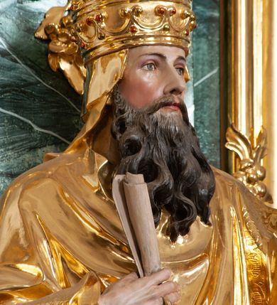 Zdjęcie nr 5: Rzeźba delikatnie ścięta z tyłu, ustawiona na niskiej podstawie. Święty zwrócony frontalnie, w kontrapoście, lewą ręką trzyma laskę zakończoną znakiem Chi Rho, w prawej, ugiętej trzyma zwój. Twarz ma pociągłą, o dużych, migdałowatych oczach, prostym nosie i małych ustach, okoloną gęstą, kręconą brodą, opadającą na pierś. Na głowie ma złoconą tiarę papieską. Ubrany jest w luźną, złoconą albę oraz złocony ornat o dekoracyjnej płaskorzeźbionej bordiurze. Polichromia ciała naturalistyczna. 