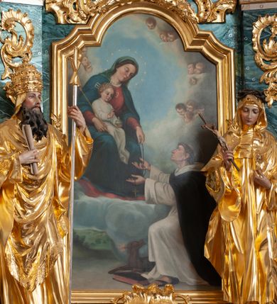 Zdjęcie nr 1: Obraz w formie stojącego prostokąta zamkniętego łukiem odcinkowym nadwieszonym z uskokiem z przedstawieniem Matki Boskiej z Dzieciątkiem przekazującej różaniec św. Dominikowi. W lewej części obrazu ukazana Maria, tronująca pośród obłoków, w pozycji siedzącej, zwrócona w trzech czwartych w lewo, pochylona. Lewą wyciągniętą przed siebie ręką podaje różaniec, prawą obejmuje Dzieciątko siedzące na jej kolanach, w dłoni trzyma berło. Maria ma owalną twarz, o okrągłych oczach skierowanych w dół, małym nosie i ustach, okoloną brązowymi włosami ukrytymi pod welonem. Wokół głowy ma nimb gwieździsty. Ubrana jest w czerwoną suknię, niebieski płaszcz zarzucony na ramiona i opadający na kolana oraz zielony welon. Dzieciątko w pozycji siedzącej, zwrócone w trzech czwartych w lewo. Prawą dłoń unosi w geście błogosławieństwa, w lewej trzyma jabłko królewskie. Twarz ma okrągłą, o dużych oczach skierowanych w dół, małym nosie i ustach, okoloną jasnymi, kręconymi, krótkimi włosami. Wokół głowy ma nimb krzyżowy. Ubrane jest w białą, długą tunikę. W prawej części obrazu, przed Marią klęczy św. Dominik, skierowany profilem w prawo, z uniesioną głową i rękami wyciągniętymi ku Marii, ujmującymi różaniec. Twarz ma szczupłą, z oczami skierowanymi w górę, dużym nosem i małymi ustami, okoloną krótkimi włosami z tonsurą na głowie. Ubrany jest w biały habit i czarny płaszcz. Na stopach ma sandały. Przed nim leży czarna księga i pies trzymający w pysku zapaloną pochodnię. W dolnej części obrazu widoczny pejzaż, w górnej niebo wypełnione chmurami i uskrzydlonymi główkami anielskimi, ułożonymi w krąg wokół Marii. 