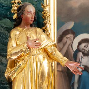 Zdjęcie nr 1: Rzeźba ścięta z tyłu, drążona, ustawiona na niskiej podstawie. Święty ukazany frontalnie, w kontrapoście, z głową skierowaną w lewo, o sylwetce delikatnie przechylonej w tył. Prawą rękę kładzie na piersi, lewą wyciąga przed siebie. Twarz ma pełną, o  wysokim czole, wąskich, migdałowatych oczach, długim, prostym nosie i pełnych, rozchylonych ustach. Włosy ma kręcone, przylegające do głowy, sięgające ramion. Ubrany jest w długą, przylegającą do ciała tunikę z kołnierzykiem, przepasaną w talii, z długimi rękawami z wywiniętymi mankietami oraz złocony płaszcz przewiązany diagonalnie przez lewe ramię, zawieszony na taśmie. Polichromia ciała naturalistyczna. 

