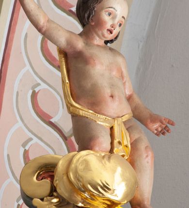 Zdjęcie nr 5: W polu o fantazyjnej, wklęsło-wypukłej formie, z uszakami płaskorzeźbione przedstawienie tronującego Boga Ojca pośród obłoków i uskrzydlonych główek anielskich. Bóg ukazany frontalnie, jako siedzący na obłoku, z ugiętymi nogami. Lewą rękę opiera na globie leżącym przy jego boku, w dłoni trzyma berło, prawą rękę wyciąga w bok. Twarz ma kwadratową, o wąskich, migdałowatych oczach, wąskim nosie i pełnych ustach, okoloną długą, siwą, rozdwajającą się brodą oraz krótkimi włosami. Wokół jego głowy nimb trójkątny. Ubrany jest w złoconą tunikę oraz złocony płaszcz zarzucony na lewe ramię i kolana, rozwiany z boku postaci. Polichromia ciała naturalistyczna. 