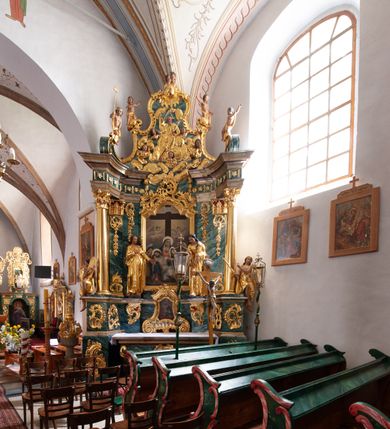 Zdjęcie nr 13: Nastawa architektoniczna, jednoosiowa, jednokondygnacyjna ze zwieńczeniem, ustawiona na dwustrefowym cokole z wyodrębnionymi prostopadłościanami, ustawionymi pod kątem. Ołtarz sarkofagowy, wklęsło-wypukły, dekorowany w narożach ornamentem roślinnym, w polu zaś rocaille'owym kartuszem. Mensa szersza, drewniana. Nastawa na planie półowalu, ujęta dwiema parami pilastrów i stojącą na ich tle parą kolumn o kapitelach kompozytowych. Podpory dźwigają pełne belkowanie, wyłamane półkoliście na ich osi, przerwane nad polem środkowym. Fryz dekorowany rozetami, cokoły rocaille'm, a trzony pilastrów rocaille'm i zwisami roślinnymi. W polu środkowym wnęka w formie stojącego prostokąta zamkniętego łukiem odcinkowym nadwieszonym z uskokiem, ujęta profilowaną ramą, zwieńczoną rocaille'owym szczytem, w polu obraz zdjęcia z krzyża. Wnękę flankują figury św. Jana Ewangelisty i św. Marii Magdaleny ustawione na rocaille'owych wspornikach. Na zewnętrzych krawędziach cokołu siedzą figury aniołów z arma Christi. Zwieńczenie o fantazyjnej, wklęsło-wypukłej formie, z uszakami i puttami, ujęte wolutami spływającymi na belkowanie, na których siedzą putta; obwiedzione rocaille'm, zakończone dwiema uskrzydlonymi główkami anielskimi. W polu płaskorzeźbione przedstawienie Boga Ojca tronującego pośród obłoków i uskrzydlonych główek anielskich. Struktura polichromowana na sposób imitujący marmoryzacje w różnych odcieniach zieleni, kolumny, ornamentyka i profile złocone, niektóre profile srebrzone. 