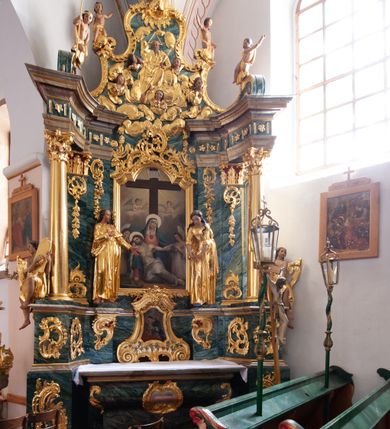 Zdjęcie nr 22: Nastawa architektoniczna, jednoosiowa, jednokondygnacyjna ze zwieńczeniem, ustawiona na dwustrefowym cokole z wyodrębnionymi prostopadłościanami, ustawionymi pod kątem. Ołtarz sarkofagowy, wklęsło-wypukły, dekorowany w narożach ornamentem roślinnym, w polu zaś rocaille'owym kartuszem. Mensa szersza, drewniana. Nastawa na planie półowalu, ujęta dwiema parami pilastrów i stojącą na ich tle parą kolumn o kapitelach kompozytowych. Podpory dźwigają pełne belkowanie, wyłamane półkoliście na ich osi, przerwane nad polem środkowym. Fryz dekorowany rozetami, cokoły rocaille'm, a trzony pilastrów rocaille'm i zwisami roślinnymi. W polu środkowym wnęka w formie stojącego prostokąta zamkniętego łukiem odcinkowym nadwieszonym z uskokiem, ujęta profilowaną ramą, zwieńczoną rocaille'owym szczytem, w polu obraz zdjęcia z krzyża. Wnękę flankują figury św. Jana Ewangelisty i św. Marii Magdaleny ustawione na rocaille'owych wspornikach. Na zewnętrzych krawędziach cokołu siedzą figury aniołów z arma Christi. Zwieńczenie o fantazyjnej, wklęsło-wypukłej formie, z uszakami i puttami, ujęte wolutami spływającymi na belkowanie, na których siedzą putta; obwiedzione rocaille'm, zakończone dwiema uskrzydlonymi główkami anielskimi. W polu płaskorzeźbione przedstawienie Boga Ojca tronującego pośród obłoków i uskrzydlonych główek anielskich. Struktura polichromowana na sposób imitujący marmoryzacje w różnych odcieniach zieleni, kolumny, ornamentyka i profile złocone, niektóre profile srebrzone. 