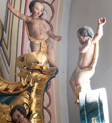 Zdjęcie nr 19: Nastawa architektoniczna, jednoosiowa, jednokondygnacyjna ze zwieńczeniem, ustawiona na dwustrefowym cokole z wyodrębnionymi prostopadłościanami, ustawionymi pod kątem. Ołtarz sarkofagowy, wklęsło-wypukły, dekorowany w narożach ornamentem roślinnym, w polu zaś rocaille'owym kartuszem. Mensa szersza, drewniana. Nastawa na planie półowalu, ujęta dwiema parami pilastrów i stojącą na ich tle parą kolumn o kapitelach kompozytowych. Podpory dźwigają pełne belkowanie, wyłamane półkoliście na ich osi, przerwane nad polem środkowym. Fryz dekorowany rozetami, cokoły rocaille'm, a trzony pilastrów rocaille'm i zwisami roślinnymi. W polu środkowym wnęka w formie stojącego prostokąta zamkniętego łukiem odcinkowym nadwieszonym z uskokiem, ujęta profilowaną ramą, zwieńczoną rocaille'owym szczytem, w polu obraz zdjęcia z krzyża. Wnękę flankują figury św. Jana Ewangelisty i św. Marii Magdaleny ustawione na rocaille'owych wspornikach. Na zewnętrzych krawędziach cokołu siedzą figury aniołów z arma Christi. Zwieńczenie o fantazyjnej, wklęsło-wypukłej formie, z uszakami i puttami, ujęte wolutami spływającymi na belkowanie, na których siedzą putta; obwiedzione rocaille'm, zakończone dwiema uskrzydlonymi główkami anielskimi. W polu płaskorzeźbione przedstawienie Boga Ojca tronującego pośród obłoków i uskrzydlonych główek anielskich. Struktura polichromowana na sposób imitujący marmoryzacje w różnych odcieniach zieleni, kolumny, ornamentyka i profile złocone, niektóre profile srebrzone. 
