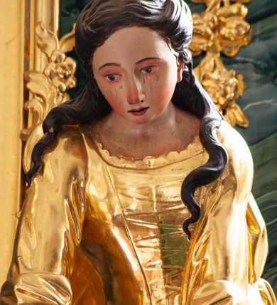 Zdjęcie nr 12: Nastawa architektoniczna, jednoosiowa, jednokondygnacyjna ze zwieńczeniem, ustawiona na dwustrefowym cokole z wyodrębnionymi prostopadłościanami, ustawionymi pod kątem. Ołtarz sarkofagowy, wklęsło-wypukły, dekorowany w narożach ornamentem roślinnym, w polu zaś rocaille'owym kartuszem. Mensa szersza, drewniana. Nastawa na planie półowalu, ujęta dwiema parami pilastrów i stojącą na ich tle parą kolumn o kapitelach kompozytowych. Podpory dźwigają pełne belkowanie, wyłamane półkoliście na ich osi, przerwane nad polem środkowym. Fryz dekorowany rozetami, cokoły rocaille'm, a trzony pilastrów rocaille'm i zwisami roślinnymi. W polu środkowym wnęka w formie stojącego prostokąta zamkniętego łukiem odcinkowym nadwieszonym z uskokiem, ujęta profilowaną ramą, zwieńczoną rocaille'owym szczytem, w polu obraz zdjęcia z krzyża. Wnękę flankują figury św. Jana Ewangelisty i św. Marii Magdaleny ustawione na rocaille'owych wspornikach. Na zewnętrzych krawędziach cokołu siedzą figury aniołów z arma Christi. Zwieńczenie o fantazyjnej, wklęsło-wypukłej formie, z uszakami i puttami, ujęte wolutami spływającymi na belkowanie, na których siedzą putta; obwiedzione rocaille'm, zakończone dwiema uskrzydlonymi główkami anielskimi. W polu płaskorzeźbione przedstawienie Boga Ojca tronującego pośród obłoków i uskrzydlonych główek anielskich. Struktura polichromowana na sposób imitujący marmoryzacje w różnych odcieniach zieleni, kolumny, ornamentyka i profile złocone, niektóre profile srebrzone. 