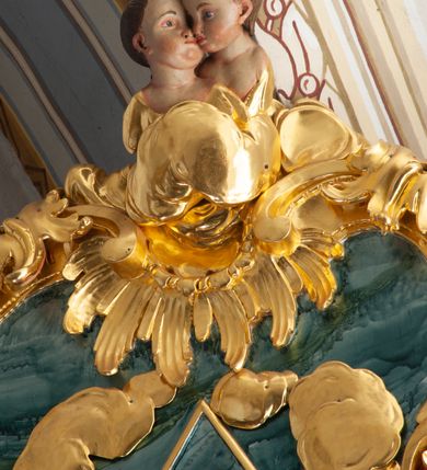 Zdjęcie nr 26: Nastawa architektoniczna, jednoosiowa, jednokondygnacyjna ze zwieńczeniem, ustawiona na dwustrefowym cokole z wyodrębnionymi prostopadłościanami, ustawionymi pod kątem. Ołtarz sarkofagowy, wklęsło-wypukły, dekorowany w narożach ornamentem roślinnym, w polu zaś rocaille&#039;owym kartuszem. Mensa szersza, drewniana. Nastawa na planie półowalu, ujęta dwiema parami pilastrów i stojącą na ich tle parą kolumn o kapitelach kompozytowych. Podpory dźwigają pełne belkowanie, wyłamane półkoliście na ich osi, przerwane nad polem środkowym. Fryz dekorowany rozetami, cokoły rocaille&#039;m, a trzony pilastrów rocaille&#039;m i zwisami roślinnymi. W polu środkowym wnęka w formie stojącego prostokąta zamkniętego łukiem odcinkowym nadwieszonym z uskokiem, ujęta profilowaną ramą, zwieńczoną rocaille&#039;owym szczytem, w polu obraz zdjęcia z krzyża. Wnękę flankują figury św. Jana Ewangelisty i św. Marii Magdaleny ustawione na rocaille&#039;owych wspornikach. Na zewnętrzych krawędziach cokołu siedzą figury aniołów z arma Christi. Zwieńczenie o fantazyjnej, wklęsło-wypukłej formie, z uszakami i puttami, ujęte wolutami spływającymi na belkowanie, na których siedzą putta; obwiedzione rocaille&#039;m, zakończone dwiema uskrzydlonymi główkami anielskimi. W polu płaskorzeźbione przedstawienie Boga Ojca tronującego pośród obłoków i uskrzydlonych główek anielskich. Struktura polichromowana na sposób imitujący marmoryzacje w różnych odcieniach zieleni, kolumny, ornamentyka i profile złocone, niektóre profile srebrzone. 