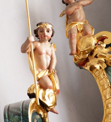 Zdjęcie nr 20: Nastawa architektoniczna, jednoosiowa, jednokondygnacyjna ze zwieńczeniem, ustawiona na dwustrefowym cokole z wyodrębnionymi prostopadłościanami, ustawionymi pod kątem. Ołtarz sarkofagowy, wklęsło-wypukły, dekorowany w narożach ornamentem roślinnym, w polu zaś rocaille'owym kartuszem. Mensa szersza, drewniana. Nastawa na planie półowalu, ujęta dwiema parami pilastrów i stojącą na ich tle parą kolumn o kapitelach kompozytowych. Podpory dźwigają pełne belkowanie, wyłamane półkoliście na ich osi, przerwane nad polem środkowym. Fryz dekorowany rozetami, cokoły rocaille'm, a trzony pilastrów rocaille'm i zwisami roślinnymi. W polu środkowym wnęka w formie stojącego prostokąta zamkniętego łukiem odcinkowym nadwieszonym z uskokiem, ujęta profilowaną ramą, zwieńczoną rocaille'owym szczytem, w polu obraz zdjęcia z krzyża. Wnękę flankują figury św. Jana Ewangelisty i św. Marii Magdaleny ustawione na rocaille'owych wspornikach. Na zewnętrzych krawędziach cokołu siedzą figury aniołów z arma Christi. Zwieńczenie o fantazyjnej, wklęsło-wypukłej formie, z uszakami i puttami, ujęte wolutami spływającymi na belkowanie, na których siedzą putta; obwiedzione rocaille'm, zakończone dwiema uskrzydlonymi główkami anielskimi. W polu płaskorzeźbione przedstawienie Boga Ojca tronującego pośród obłoków i uskrzydlonych główek anielskich. Struktura polichromowana na sposób imitujący marmoryzacje w różnych odcieniach zieleni, kolumny, ornamentyka i profile złocone, niektóre profile srebrzone. 