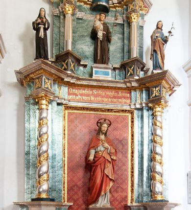 Zdjęcie nr 2: Nastawa architektoniczna, jednoosiowa, dwukondygnacyjna ze zwieńczeniem, ustawiona na dwustrefowym cokole z wyłamanymi pod kątem prostopadłościanami. Ołtarz sarkofagowy, wklęsło-wypukły, na wysokim cokole, dekorowany w narożach ornamentem roślinnym i rocaille'owym kartuszem w polu. Mensa szersza od ołtarza, drewniana. Nastawa ujęta parą kolumn o skręconych trzonach zdobionych wicią roślinną, podtrzymujących pełne belkowanie, wyłamane na ich osi pod kątem. Fryz i cokół na linii kolumn dekorowany płycinami z ornamentem roślinnym, na belkowaniu ustawione figury św. Teresy i św. Józefa. W środkowej części fryzu napis „O najsladsie Srdce môjho Ježiša / učíň, aby som Ta vždy viac a viac milovah”. Całe pole główne wypełnia wnęka ujęta ramą dekorowaną ornamentem roślinnym, z tłem złożonym z kratki i krzyży. Na jej tle, na cokole ustawiona figura Najświętszego Serca Jezusa. Druga kondygnacja węższa, ustawiona na cokole z wyłamanymi pod kątem prostopadłościanami; ujęta parą kolumn podtrzymującą pełne belkowanie, wyłamane na ich osi pod kątem, na nim dwie figurki aniołów. W polu figura św. Antoniego Padewskiego ustawiona na cokole. Zwieńczenie w formie leżącego prostokąta zamkniętego gzymsem przyjmującym kształt łuku półkolistego, dekorowanego ornamentem roślinnym, zwieńczonego krzyżem. W polu medalion z monogramem IHS w glorii promienistej, na wypukłym, półokrągłym cokole. Struktura polichromowana na sposób imitujący marmoryzację w kolorze zielono-białym, z czerwonymi detalami, kolumny, profile oraz ornamentyka złocone i srebrzone.  
