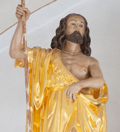 Zdjęcie nr 1: Rzeźba ścięta z tyłu. Postać Jana Chrzciciela ukazana frontalnie, w wykroku. Prawa ręka ugięta i uniesiona, trzyma laskę zakończoną krzyżem, lewa ugięta i opuszczona, trzyma z przodu połę płaszcza. Święty ma kwadratową twarz, o migdałowatych oczach, małym nosie i ustach, okoloną krótką brodą oraz falowanymi, brązowymi włosami sięgającymi ramion. Ubrany jest w złoconą melotę, zawiązaną diagonalnie przez prawe ramię, odsłaniającą część wychudzonego torsu. Przy prawej nodze świętego srebrzony baranek. Polichromia ciała naturalistyczna. 

