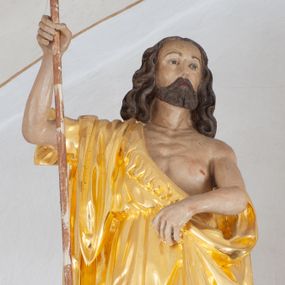 Zdjęcie nr 1: Rzeźba ścięta z tyłu. Postać Jana Chrzciciela ukazana frontalnie, w wykroku. Prawa ręka ugięta i uniesiona, trzyma laskę zakończoną krzyżem, lewa ugięta i opuszczona, trzyma z przodu połę płaszcza. Święty ma kwadratową twarz, o migdałowatych oczach, małym nosie i ustach, okoloną krótką brodą oraz falowanymi, brązowymi włosami sięgającymi ramion. Ubrany jest w złoconą melotę, zawiązaną diagonalnie przez prawe ramię, odsłaniającą część wychudzonego torsu. Przy prawej nodze świętego srebrzony baranek. Polichromia ciała naturalistyczna. 

