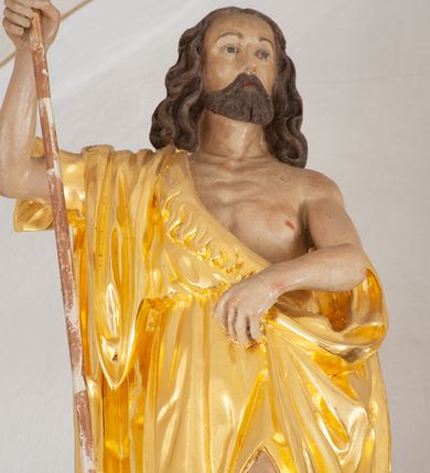 Zdjęcie nr 2: Rzeźba ścięta z tyłu. Postać Jana Chrzciciela ukazana frontalnie, w wykroku. Prawa ręka ugięta i uniesiona, trzyma laskę zakończoną krzyżem, lewa ugięta i opuszczona, trzyma z przodu połę płaszcza. Święty ma kwadratową twarz, o migdałowatych oczach, małym nosie i ustach, okoloną krótką brodą oraz falowanymi, brązowymi włosami sięgającymi ramion. Ubrany jest w złoconą melotę, zawiązaną diagonalnie przez prawe ramię, odsłaniającą część wychudzonego torsu. Przy prawej nodze świętego srebrzony baranek. Polichromia ciała naturalistyczna. 

