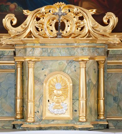 Zdjęcie nr 12: Nastawa architektoniczna, jednoosiowa, jednokondygnacyjna ze zwieńczeniem, ustawiona na dwustrefowym, szerszym cokole, z wyodrębnionymi dwiema parami prostopadłościanów, zwróconymi pod kątem. Ołtarz drewniany, sarkofagowy, wklęsło-wypukły, ustawiony na cokole. Mensa drewniana. Na ołtarzu tabernakulum w formie drewnianej skrzynki, ustawionej na cokole, flankowanej dwiema parami kolumienek, podtrzymujących belkowanie. Drzwiczki w kształcie stojącego prostokąta zamkniętego łukiem półkolistym z przedstawieniem kielicha z hostią w glorii. Całość zwieńczona szczytem utworzonym z rocaille'u i akantu. Nastawa ujęta parą kolumn podtrzymujących pełne belkowanie, z silnie wysuniętym gzymsem, wyłamane pod kątem na ich osi. W partii fryzu kartusz ujęty ornamentem roślinnym z monogramem św. Anny. Na belkowaniu ustawione figury św. Jana Chrzciciela i św. Sebastiana. W polu środkowym wnęka w formie stojącego prostokąta w wąskiej ramie, w niej obraz św. Anny Samotrzeć, w osobnej ramie dekorowanej płaskorzeźbionym wieńcem laurowym. Kondygnację flankują dwie figury aniołów ustawione na krawędzi cokołu nastawy. Zwieńczenie w formie stojącego prostokąta flankowane pilastrami podtrzymującymi pełne belkowanie wyłamane na ich osi. Trzony dekorowane zwisami. Całość zakończona szczytem w postaci stylizowanego anthemionu z karbowaną wstęgą. W polu obraz ubiczowanego Chrystusa w formie kwadratu, w ramie oraz pod nim prześwit z okrągłym oknem witrażowym w ramie o kształcie kwadratu. Zwieńczenie ujęte uszami utworzonymi z akantu i karbowanej wstęgi. Struktura polichromowana na sposób imitujący marmoryzację w kolorze żółto-zielonym, z czerwonymi detalami, kolumny, ornamentyka i profile złocone, część profili srebrzona. 