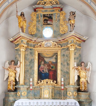 Zdjęcie nr 1: Nastawa architektoniczna, jednoosiowa, jednokondygnacyjna ze zwieńczeniem, ustawiona na dwustrefowym, szerszym cokole, z wyodrębnionymi dwiema parami prostopadłościanów, zwróconymi pod kątem. Ołtarz drewniany, sarkofagowy, wklęsło-wypukły, ustawiony na cokole. Mensa drewniana. Na ołtarzu tabernakulum w formie drewnianej skrzynki, ustawionej na cokole, flankowanej dwiema parami kolumienek, podtrzymujących belkowanie. Drzwiczki w kształcie stojącego prostokąta zamkniętego łukiem półkolistym z przedstawieniem kielicha z hostią w glorii. Całość zwieńczona szczytem utworzonym z rocaille'u i akantu. Nastawa ujęta parą kolumn podtrzymujących pełne belkowanie, z silnie wysuniętym gzymsem, wyłamane pod kątem na ich osi. W partii fryzu kartusz ujęty ornamentem roślinnym z monogramem św. Anny. Na belkowaniu ustawione figury św. Jana Chrzciciela i św. Sebastiana. W polu środkowym wnęka w formie stojącego prostokąta w wąskiej ramie, w niej obraz św. Anny Samotrzeć, w osobnej ramie dekorowanej płaskorzeźbionym wieńcem laurowym. Kondygnację flankują dwie figury aniołów ustawione na krawędzi cokołu nastawy. Zwieńczenie w formie stojącego prostokąta flankowane pilastrami podtrzymującymi pełne belkowanie wyłamane na ich osi. Trzony dekorowane zwisami. Całość zakończona szczytem w postaci stylizowanego anthemionu z karbowaną wstęgą. W polu obraz ubiczowanego Chrystusa w formie kwadratu, w ramie oraz pod nim prześwit z okrągłym oknem witrażowym w ramie o kształcie kwadratu. Zwieńczenie ujęte uszami utworzonymi z akantu i karbowanej wstęgi. Struktura polichromowana na sposób imitujący marmoryzację w kolorze żółto-zielonym, z czerwonymi detalami, kolumny, ornamentyka i profile złocone, część profili srebrzona. 