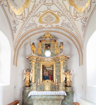 Zdjęcie nr 2: Nastawa architektoniczna, jednoosiowa, jednokondygnacyjna ze zwieńczeniem, ustawiona na dwustrefowym, szerszym cokole, z wyodrębnionymi dwiema parami prostopadłościanów, zwróconymi pod kątem. Ołtarz drewniany, sarkofagowy, wklęsło-wypukły, ustawiony na cokole. Mensa drewniana. Na ołtarzu tabernakulum w formie drewnianej skrzynki, ustawionej na cokole, flankowanej dwiema parami kolumienek, podtrzymujących belkowanie. Drzwiczki w kształcie stojącego prostokąta zamkniętego łukiem półkolistym z przedstawieniem kielicha z hostią w glorii. Całość zwieńczona szczytem utworzonym z rocaille'u i akantu. Nastawa ujęta parą kolumn podtrzymujących pełne belkowanie, z silnie wysuniętym gzymsem, wyłamane pod kątem na ich osi. W partii fryzu kartusz ujęty ornamentem roślinnym z monogramem św. Anny. Na belkowaniu ustawione figury św. Jana Chrzciciela i św. Sebastiana. W polu środkowym wnęka w formie stojącego prostokąta w wąskiej ramie, w niej obraz św. Anny Samotrzeć, w osobnej ramie dekorowanej płaskorzeźbionym wieńcem laurowym. Kondygnację flankują dwie figury aniołów ustawione na krawędzi cokołu nastawy. Zwieńczenie w formie stojącego prostokąta flankowane pilastrami podtrzymującymi pełne belkowanie wyłamane na ich osi. Trzony dekorowane zwisami. Całość zakończona szczytem w postaci stylizowanego anthemionu z karbowaną wstęgą. W polu obraz ubiczowanego Chrystusa w formie kwadratu, w ramie oraz pod nim prześwit z okrągłym oknem witrażowym w ramie o kształcie kwadratu. Zwieńczenie ujęte uszami utworzonymi z akantu i karbowanej wstęgi. Struktura polichromowana na sposób imitujący marmoryzację w kolorze żółto-zielonym, z czerwonymi detalami, kolumny, ornamentyka i profile złocone, część profili srebrzona. 