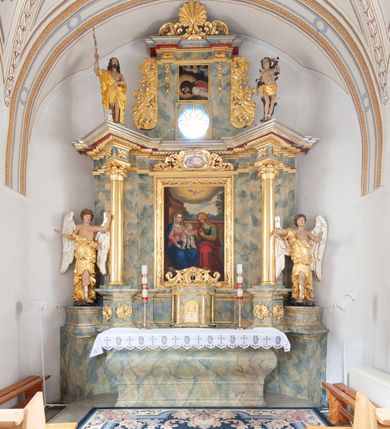 Zdjęcie nr 10: Nastawa architektoniczna, jednoosiowa, jednokondygnacyjna ze zwieńczeniem, ustawiona na dwustrefowym, szerszym cokole, z wyodrębnionymi dwiema parami prostopadłościanów, zwróconymi pod kątem. Ołtarz drewniany, sarkofagowy, wklęsło-wypukły, ustawiony na cokole. Mensa drewniana. Na ołtarzu tabernakulum w formie drewnianej skrzynki, ustawionej na cokole, flankowanej dwiema parami kolumienek, podtrzymujących belkowanie. Drzwiczki w kształcie stojącego prostokąta zamkniętego łukiem półkolistym z przedstawieniem kielicha z hostią w glorii. Całość zwieńczona szczytem utworzonym z rocaille'u i akantu. Nastawa ujęta parą kolumn podtrzymujących pełne belkowanie, z silnie wysuniętym gzymsem, wyłamane pod kątem na ich osi. W partii fryzu kartusz ujęty ornamentem roślinnym z monogramem św. Anny. Na belkowaniu ustawione figury św. Jana Chrzciciela i św. Sebastiana. W polu środkowym wnęka w formie stojącego prostokąta w wąskiej ramie, w niej obraz św. Anny Samotrzeć, w osobnej ramie dekorowanej płaskorzeźbionym wieńcem laurowym. Kondygnację flankują dwie figury aniołów ustawione na krawędzi cokołu nastawy. Zwieńczenie w formie stojącego prostokąta flankowane pilastrami podtrzymującymi pełne belkowanie wyłamane na ich osi. Trzony dekorowane zwisami. Całość zakończona szczytem w postaci stylizowanego anthemionu z karbowaną wstęgą. W polu obraz ubiczowanego Chrystusa w formie kwadratu, w ramie oraz pod nim prześwit z okrągłym oknem witrażowym w ramie o kształcie kwadratu. Zwieńczenie ujęte uszami utworzonymi z akantu i karbowanej wstęgi. Struktura polichromowana na sposób imitujący marmoryzację w kolorze żółto-zielonym, z czerwonymi detalami, kolumny, ornamentyka i profile złocone, część profili srebrzona. 