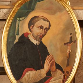 Zdjęcie nr 1: Obraz w kształcie stojącego owalu, ujęty złoconą ramą dekorowaną akantowymi wolutami oraz rocaille'm. W centrum kompozycji ukazany św. Stanisław Kazimierczyk przedstawiony w półpostaci z ciałem zwróconym w lewą stronę. Postać klęczy przed pulpitem nakrytym czerwoną tkaniną, na którym ustawiono krucyfiks, otwartą księgę oraz czaszkę. Ręce postaci złożone w geście modlitwy, głowa pochylona nieco do przodu. Święty został przedstawiony jako dojrzały mężczyzna o szczupłej twarzy z dużymi, ciemnymi oczami oraz pełnymi ustami. Włosy z tonsurą jasno-brązowe. Taki sam, krótki zarost. Wokół głowy widoczny nimb. Postać ubrana jest w strój kanoników regularnych: czarną sutannę, białą komżę oraz czarny mucet z czerwonym podbiciem. W tle przedstawione szaro-złote obłoki oraz fragment podwieszonej kotary w kolorze morskiej zieleni (z lewej strony kompozycji).