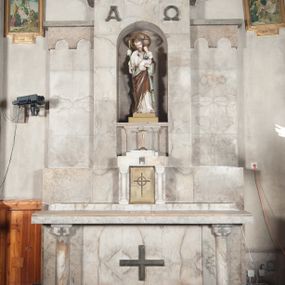 Zdjęcie nr 1: Ołtarz przyścienny, trójosiowy, jednokondygnacyjny, o formach architektonicznych, ustawiony na jednostopniowym podwyższeniu. Mensa kamienna, wsparta na dwóch półkolumnach o gładkich trzonach i kostkowych kapitelach z motywem krzyża greckiego. Antepedium gładkie, w formie alabastrowej płyty z umieszczonym centralnie metalowym krzyżem. Retabulum umieszczone na wysokim cokole. Oś środkowa nieco wyższa od osi skrajnych i wysunięta do przodu mieści zamkniętą półkoliście niszę z ustawioną na postumencie figurą przedstawiającą św. Józefa z Dzieciątkiem Jezus. Powyżej niszy litery „Α” (álfa) i „Ω” (oméga). W zwieńczeniu płaskorzeźbione przedstawienie kielicha z hostią ujętego wieńcem, w okrągłym polu zakończonym krzyżem. Osie skrajne nastawy nieco niższe, zwieńczone fryzem arkadowym. W osi ołtarza alabastrowe tabernakulum ujęte parą półkolumn o gładkich trzonach i kostkowych kapitelach. Drzwiczki metalowe z motywem krzyża.

