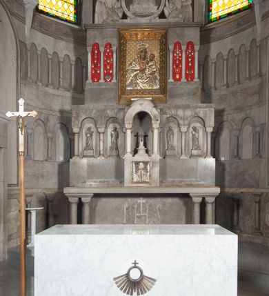 Zdjęcie nr 10: Ołtarz przyścienny, architektoniczny, pięcioosiowy, dwukondygnacyjny ze zwieńczeniem. Mensa kamienna, w formie stołu wsparta na parach kolumn o kostkowych kapitelach. Antepedium również kamienne, z umieszczonym w centrum monogramem IHS zwieńczonym krzyżem. Kondygnacja pierwsza artykułowana pięcioma arkadami ujętymi kolumienkami o kostkowych kapitelach. W arkadach umieszczone płaskorzeźbione postaci czterech ewangelistów: Jana, Marka, Łukasza i Mateusza. W osi środkowej prostopadłościenne, alabastrowe tabernakulum z tronem wystawienia nakrytym kamiennym baldachimem w formie kopuły wspartej na czterech kolumnach o kostkowych kapitelach. Na drzwiczkach umieszczony krzyż na tle glorii promienistej flankowany przez postaci klęczących aniołów. Kondygnacja druga artykułowana arkadami wspartymi na kolumnach o kostkowych kapitelach. W arkadach umieszczone dary wotywne. W osi środkowej znajduje się obraz Matki Boskiej z Dzieciątkiem w prostokątnej, złotej ramie. Struktura zwieńczona profilowanym gzymsem, ponad którym umieszczono płaskorzeźbione przedstawienie Baranka Apokaliptycznego ujętego medalionem zwieńczonym krzyżem oraz flankowanego przez postaci dwóch klęczących aniołów.
