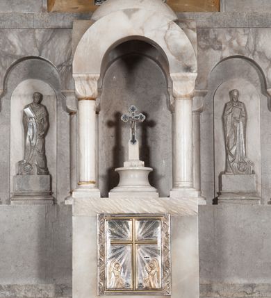 Zdjęcie nr 11: Ołtarz przyścienny, architektoniczny, pięcioosiowy, dwukondygnacyjny ze zwieńczeniem. Mensa kamienna, w formie stołu wsparta na parach kolumn o kostkowych kapitelach. Antepedium również kamienne, z umieszczonym w centrum monogramem IHS zwieńczonym krzyżem. Kondygnacja pierwsza artykułowana pięcioma arkadami ujętymi kolumienkami o kostkowych kapitelach. W arkadach umieszczone płaskorzeźbione postaci czterech ewangelistów: Jana, Marka, Łukasza i Mateusza. W osi środkowej prostopadłościenne, alabastrowe tabernakulum z tronem wystawienia nakrytym kamiennym baldachimem w formie kopuły wspartej na czterech kolumnach o kostkowych kapitelach. Na drzwiczkach umieszczony krzyż na tle glorii promienistej flankowany przez postaci klęczących aniołów. Kondygnacja druga artykułowana arkadami wspartymi na kolumnach o kostkowych kapitelach. W arkadach umieszczone dary wotywne. W osi środkowej znajduje się obraz Matki Boskiej z Dzieciątkiem w prostokątnej, złotej ramie. Struktura zwieńczona profilowanym gzymsem, ponad którym umieszczono płaskorzeźbione przedstawienie Baranka Apokaliptycznego ujętego medalionem zwieńczonym krzyżem oraz flankowanego przez postaci dwóch klęczących aniołów.
