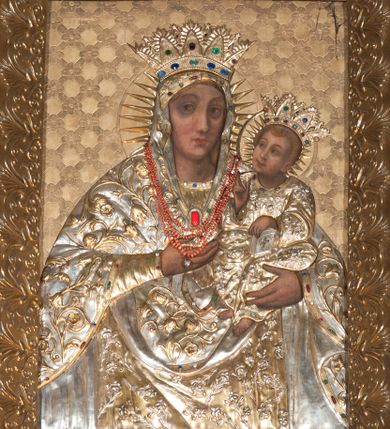 Zdjęcie nr 1: Obraz w kształcie stojącego prostokąta. Matka Boska została ukazana frontalnie, w półpostaci z Dzieciątkiem, które trzyma na swoim lewym ramieniu. Głowa Marii zwrócona w lewo, spojrzenie skierowane na wprost. Jej twarz jest owalna o dużych, ciemnych oczach, długim nosie, niewielkich, czerwonych ustach oraz wydatnym podbródku. Prawa ręka Marii, ugięta w łokciu i uniesiona ku górze wskazuje na Dzieciątko. Postać ubrana jest w jasnozieloną suknię oraz narzucony na głowę ciemnozielony welon opadający na ramiona Marii. Pod szyją spięty owalną, złotą broszą. Głowa Dzieciątka ujęta w trzech czwartych i uniesiona delikatnie w górę ku twarzy Marii. Włosy jasne układające się w loki. Twarz pełna o zarumienionych policzkach, dużych, szeroko otwartych oczach spoglądających na Marię oraz długim, prostym nosie. Dzieciątko prawą ręką błogosławi, jego lewa ręka spoczywa na zamkniętej księdze z motywem krzyża na okładce. Postać ubrana jest w długą, jasnozieloną tunikę o długich rękawach obszytych złotą lamówką. Na otoczonych nimbem oraz promieniami głowach Marii i Dzieciątka znajdują się złocone i kameryzowane korony otwarte. Tło obrazu jest jednolicie złocone z motywem ukośnie ustawionej kratki z kwiatami na przecięciach. Na postaci Marii oraz Dzieciątka nałożone srebrzone i złocone, blaszane sukienki dekorowane motywami kwiatowymi (lilii oraz róż) oraz kameryzacją. Obraz ujęty szeroką, złoconą ramą dekorowaną motywem palmet. 