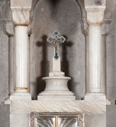 Zdjęcie nr 8: Płaskorzeźbione przedstawienia ewangelistów ukazanych całopostaciowo, w pozycji stojącej, umieszczone na prostopadłościennych, profilowanych u podstawy postumentach. Święty Jan Ewangelista ujęty jako młody, długowłosy mężczyzna z ciałem zwróconym w trzech czwartych w lewo. Głowa pochylona do dołu, twarz szczupła, o regularnych rysach i prostym nosie. Święty w swojej lewej ręce trzyma otwartą księgę, prawą dłonią wskazuje na zapisany w niej tekst. Postać ubrana w długą, obszerną szatę o szerokich rękawach i luźno przerzucony przez prawe ramię płaszcz. U stóp świętego z lewej strony kompozycji przedstawiony atrybut św. Jana – orzeł. Święty Marek został ukazany frontalnie, jako dojrzały, krótkowłosy mężczyzna. Głowa przechylona nieznacznie w lewą stronę, twarz okrągła z wyraźnie zaznaczonym, prostym nosem. Święty w swojej prawej, ugiętej w łokciu ręce trzyma zamkniętą księgę. Lewa ręka o wyraźnie zaznaczonej muskulaturze opuszczona wzdłuż ciała, dłoń wsparta na udzie. Postać ubrana w długą szatę o krótkim rękawie oraz obszerny, luźno zarzucony na prawe ramię płaszcz. U stóp świętego, z lewej strony kompozycji ukazany atrybut w postaci uskrzydlonej lwiej głowy. Święty Łukasz został przedstawiony frontalnie jako dojrzały, krótkowłosy mężczyzna o owalnej twarzy i krótkiej brodzie. Postać oburącz trzyma zamkniętą księgę. Święty ubrany jest w długą szatę oraz okrywający całą sylwetkę płaszcz. U stóp postaci z prawej strony kompozycji przedstawiono atrybut św. Łukasza w postaci uskrzydlonej głowy wołu. Ostatni z ewangelistów – św. Mateusz został ukazany ciałem zwróconym w trzech czwartych w prawo i głową ujętą z profilu oraz pochyloną do dołu. Ewangelistę przedstawiono jako starszego mężczyznę o dłuższych, falowanych i przerzedzonych nad czołem włosach i krótkiej brodzie. Postać ubrana w długą szatę oraz obszerny płaszcz w obu rękach trzyma zamkniętą księgę. U stóp św. Mateusza, z prawej strony kompozycji przedstawiono jego atrybut – uskrzydloną głowę anioła. 