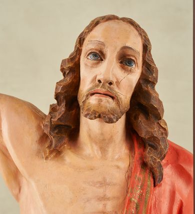 Zdjęcie nr 6: Figura pełnoplastyczna, ustawiona na niewysokim, prostopadłościennym postumencie o ściętych narożach. Chrystus przedstawiony całopostaciowo, frontalnie, w lekkim kontrapoście. Głowa nieznacznie uniesiona do góry, prawa ręką wyciągnięta ku górze, lewa wsparta na drzewcu chorągwi Zmartwychwstania. Twarz Zbawiciela szczupła, wydłużona o wyraźnych rysach. Duże, głęboko osadzone, szeroko otwarte oczy skierowane są ku górze. Wydatny, prosty nos oraz delikatnie zaznaczone czerwienią usta. Długie, brązowe włosy opadające w lokach na ramiona i plecy postaci. Na twarzy widoczny krótki, brązowy zarost. Odsłonięta klatka piersiowa z wyraźnie zaznaczoną muskulaturą oraz widoczną raną w boku. Na lewe ramię postaci luźno zarzucony obszerny, czerwony płaszcz ze złotą lamówką. Spod szat widoczne bose stopy. Czerwona chorągiew na długim, brązowym drzewcu zakończonym krzyżem. Figura w pełni polichromowana.