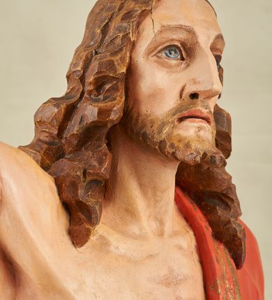 Zdjęcie nr 2: Figura pełnoplastyczna, ustawiona na niewysokim, prostopadłościennym postumencie o ściętych narożach. Chrystus przedstawiony całopostaciowo, frontalnie, w lekkim kontrapoście. Głowa nieznacznie uniesiona do góry, prawa ręką wyciągnięta ku górze, lewa wsparta na drzewcu chorągwi Zmartwychwstania. Twarz Zbawiciela szczupła, wydłużona o wyraźnych rysach. Duże, głęboko osadzone, szeroko otwarte oczy skierowane są ku górze. Wydatny, prosty nos oraz delikatnie zaznaczone czerwienią usta. Długie, brązowe włosy opadające w lokach na ramiona i plecy postaci. Na twarzy widoczny krótki, brązowy zarost. Odsłonięta klatka piersiowa z wyraźnie zaznaczoną muskulaturą oraz widoczną raną w boku. Na lewe ramię postaci luźno zarzucony obszerny, czerwony płaszcz ze złotą lamówką. Spod szat widoczne bose stopy. Czerwona chorągiew na długim, brązowym drzewcu zakończonym krzyżem. Figura w pełni polichromowana.