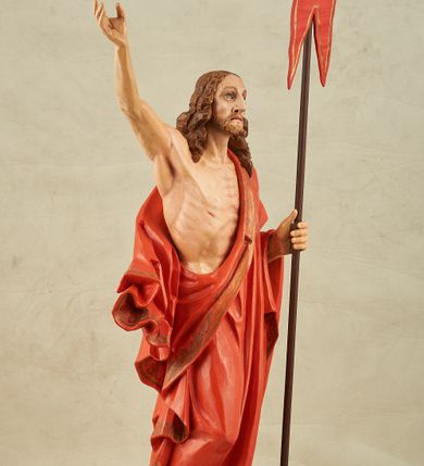Zdjęcie nr 8: Figura pełnoplastyczna, ustawiona na niewysokim, prostopadłościennym postumencie o ściętych narożach. Chrystus przedstawiony całopostaciowo, frontalnie, w lekkim kontrapoście. Głowa nieznacznie uniesiona do góry, prawa ręką wyciągnięta ku górze, lewa wsparta na drzewcu chorągwi Zmartwychwstania. Twarz Zbawiciela szczupła, wydłużona o wyraźnych rysach. Duże, głęboko osadzone, szeroko otwarte oczy skierowane są ku górze. Wydatny, prosty nos oraz delikatnie zaznaczone czerwienią usta. Długie, brązowe włosy opadające w lokach na ramiona i plecy postaci. Na twarzy widoczny krótki, brązowy zarost. Odsłonięta klatka piersiowa z wyraźnie zaznaczoną muskulaturą oraz widoczną raną w boku. Na lewe ramię postaci luźno zarzucony obszerny, czerwony płaszcz ze złotą lamówką. Spod szat widoczne bose stopy. Czerwona chorągiew na długim, brązowym drzewcu zakończonym krzyżem. Figura w pełni polichromowana.