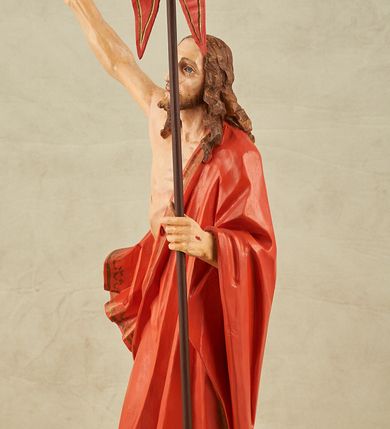 Zdjęcie nr 11: Figura pełnoplastyczna, ustawiona na niewysokim, prostopadłościennym postumencie o ściętych narożach. Chrystus przedstawiony całopostaciowo, frontalnie, w lekkim kontrapoście. Głowa nieznacznie uniesiona do góry, prawa ręką wyciągnięta ku górze, lewa wsparta na drzewcu chorągwi Zmartwychwstania. Twarz Zbawiciela szczupła, wydłużona o wyraźnych rysach. Duże, głęboko osadzone, szeroko otwarte oczy skierowane są ku górze. Wydatny, prosty nos oraz delikatnie zaznaczone czerwienią usta. Długie, brązowe włosy opadające w lokach na ramiona i plecy postaci. Na twarzy widoczny krótki, brązowy zarost. Odsłonięta klatka piersiowa z wyraźnie zaznaczoną muskulaturą oraz widoczną raną w boku. Na lewe ramię postaci luźno zarzucony obszerny, czerwony płaszcz ze złotą lamówką. Spod szat widoczne bose stopy. Czerwona chorągiew na długim, brązowym drzewcu zakończonym krzyżem. Figura w pełni polichromowana.