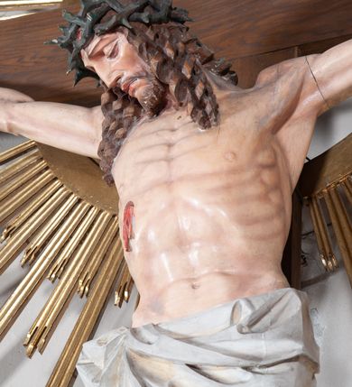 Zdjęcie nr 3: Pełnoplastyczna, polichromowana figura ukrzyżowanego Chrystusa w typie Cristo morte na drewnianym krzyżu umieszczonym na tle złoconej glorii promienistej o alternowanych promieniach. Ciało Chrystusa wyprostowane, szczupłe z silnie zaznaczoną muskulaturą. Ramiona wyprostowane, uniesione nieznacznie do góry, stopy przebite jednym gwoździem. Głowa Chrystusa pochylona lekko do przodu i złożona na prawym ramieniu postaci. Twarz szczupła, podłużna, z wyraźnie zaznaczonymi kośćmi policzkowymi. Głęboko osadzone, duże oczy zamknięte; nos prosty, wydatny. Głowę Chrystusa w cierniowej koronie okalają długie, brązowe włosy układające się w spiralnie skręcone loki; zarost krótki, brązowy. Na prawym boku postaci oraz stopach i dłoniach widoczne krwawiące rany. Wokół bioder Chrystusa udrapowane białe perizonium przewiązane na prawym boku w wydatny węzeł i spływające obfitymi, ekspresyjnymi fałdami do dołu. U szczytu pionowej belki krzyża umieszczona biała banderola z napisem: INRI.