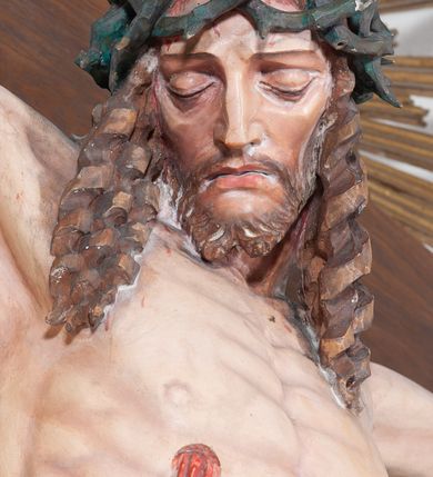Zdjęcie nr 5: Pełnoplastyczna, polichromowana figura ukrzyżowanego Chrystusa w typie Cristo morte na drewnianym krzyżu umieszczonym na tle złoconej glorii promienistej o alternowanych promieniach. Ciało Chrystusa wyprostowane, szczupłe z silnie zaznaczoną muskulaturą. Ramiona wyprostowane, uniesione nieznacznie do góry, stopy przebite jednym gwoździem. Głowa Chrystusa pochylona lekko do przodu i złożona na prawym ramieniu postaci. Twarz szczupła, podłużna, z wyraźnie zaznaczonymi kośćmi policzkowymi. Głęboko osadzone, duże oczy zamknięte; nos prosty, wydatny. Głowę Chrystusa w cierniowej koronie okalają długie, brązowe włosy układające się w spiralnie skręcone loki; zarost krótki, brązowy. Na prawym boku postaci oraz stopach i dłoniach widoczne krwawiące rany. Wokół bioder Chrystusa udrapowane białe perizonium przewiązane na prawym boku w wydatny węzeł i spływające obfitymi, ekspresyjnymi fałdami do dołu. U szczytu pionowej belki krzyża umieszczona biała banderola z napisem: INRI.