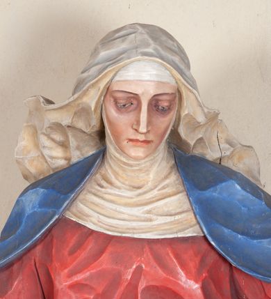 Zdjęcie nr 8: Rzeźba ustawiona na niewysokim, prostopadłościennym postumencie oraz na konsoli w kształcie fragmentu pilastra o kanelowanym trzonie i kapitelu dekorowanego motywem wolich oczu. Na tle krzyża z luźno przewieszoną przez poziomą belkę białą tkaniną ukazani Maria oraz martwy Chrystus. Jezus o szczupłym, muskularnym ciele z widocznymi śladami męki ukazany w pozycji półleżącej z torsem i ramionami wspartymi o postać Marii. Ręce ułożone luźno wzdłuż ciała. Głowa Chrystusa opada na prawe ramię postaci; twarz szczupła z wyraźnie zarysowanymi kośćmi policzkowymi, oczy zamknięte. Długie, brązowe włosy z przedziałkiem pośrodku głowy skręcają się w spiralne loki. Na twarzy krótki zarost. Wokół bioder Chrystusa luźno owinięte białe perizonium. Maria ukazana w pozycji klęczącej z rękoma uniesionymi na boki w dynamicznym geście. Głowa pochylona nieznacznie do dołu, w kierunku ciała Chrystusa. Twarz Marii szczupła, owalna z głęboko osadzonymi, dużymi oczami oraz wydatnym, prostym nosem. Postać ubrana jest w czerwoną suknię z długimi rękawami, niebieski płaszcz oraz białą chustę z podwiką wokół szyi. Po lewej stronie kompozycji, spod sukni widoczna jest bosa stopa.  