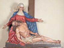 Zdjęcie nr 1: Rzeźba ustawiona na niewysokim, prostopadłościennym postumencie oraz na konsoli w kształcie fragmentu pilastra o kanelowanym trzonie i kapitelu dekorowanego motywem wolich oczu. Na tle krzyża z luźno przewieszoną przez poziomą belkę białą tkaniną ukazani Maria oraz martwy Chrystus. Jezus o szczupłym, muskularnym ciele z widocznymi śladami męki ukazany w pozycji półleżącej z torsem i ramionami wspartymi o postać Marii. Ręce ułożone luźno wzdłuż ciała. Głowa Chrystusa opada na prawe ramię postaci; twarz szczupła z wyraźnie zarysowanymi kośćmi policzkowymi, oczy zamknięte. Długie, brązowe włosy z przedziałkiem pośrodku głowy skręcają się w spiralne loki. Na twarzy krótki zarost. Wokół bioder Chrystusa luźno owinięte białe perizonium. Maria ukazana w pozycji klęczącej z rękoma uniesionymi na boki w dynamicznym geście. Głowa pochylona nieznacznie do dołu, w kierunku ciała Chrystusa. Twarz Marii szczupła, owalna z głęboko osadzonymi, dużymi oczami oraz wydatnym, prostym nosem. Postać ubrana jest w czerwoną suknię z długimi rękawami, niebieski płaszcz oraz białą chustę z podwiką wokół szyi. Po lewej stronie kompozycji, spod sukni widoczna jest bosa stopa.  